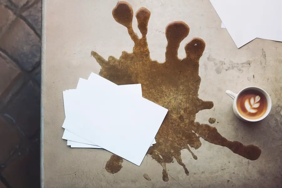 Umgekippter Becher, Kaffee läuft über Papiere auf dem Tisch