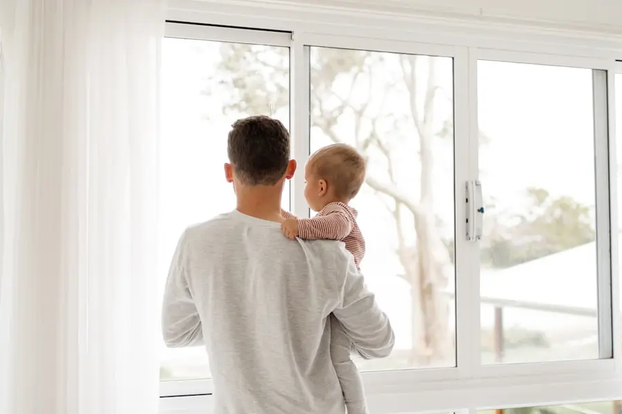 Vater steht mit seinem Kind auf dem Arm am Fenster